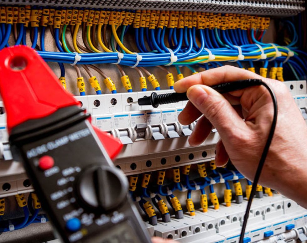 Electrician using a multimeter to test a switchboard for faults